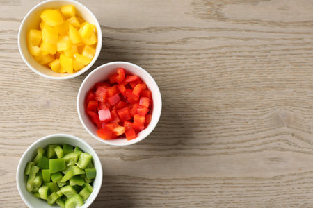 Pieces of fresh colorful bell peppers in bowls on wooden table, flat lay. Space for textの写真素材