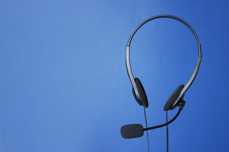 Headset with microphone in air on blue background, space for text