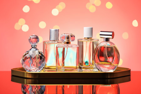 Many different perfume bottles on mirror surface against coral background with blurred lights, closeupの写真素材