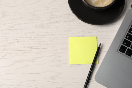 Sticky note, pen, coffee and laptop on white wooden table, above view. Space for textの写真素材
