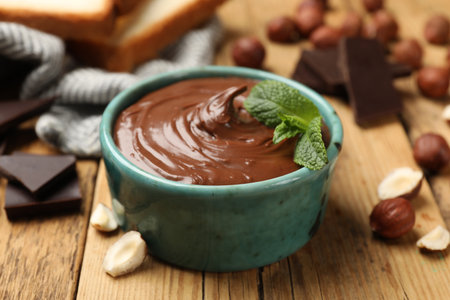 Tasty hazelnut spread with mint, chocolate pieces and nuts on wooden table, closeupの写真素材