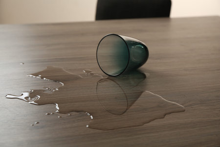 Overturned glass and spilled water on wooden tableの写真素材