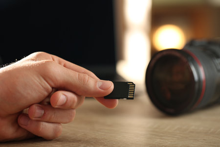 Man with SD memory card at wooden table indoors, closeupの写真素材