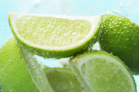 Refreshing soda water with slices of lime and ice in glass on light blue background, closeupの写真素材