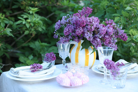 Beautiful lilac flowers, zephyrs, plates, cutlery and glasses on table in gardenの写真素材