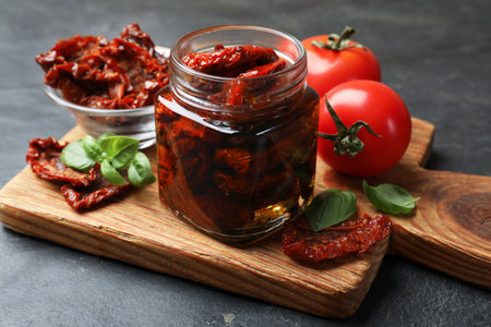 Tasty sun dried tomatoes and fresh vegetables on black table, closeupの写真素材