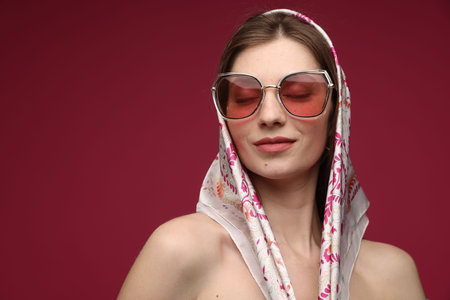 Fashionable portrait of beautiful woman in stylish outfit on dark red background. Space for textの写真素材