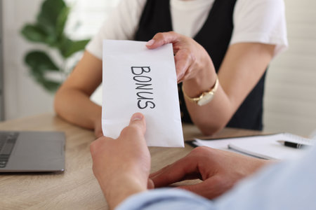 Boss giving envelope with word bonus to employee in office, closeupの写真素材