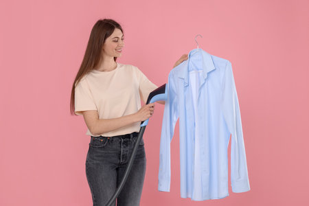 Smiling woman steaming shirt on pink backgroundの写真素材