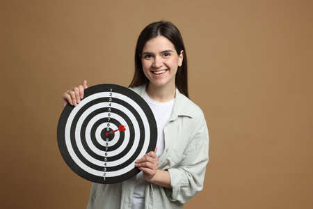 Targeting. Smiling woman with dart board and arrow on beige backgroundの写真素材