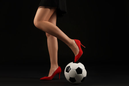 Woman in high heeled shoes with soccer ball on dark background, closeupの写真素材