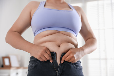 Overweight woman trying to put on tight jeans at home, closeupのeditorial素材
