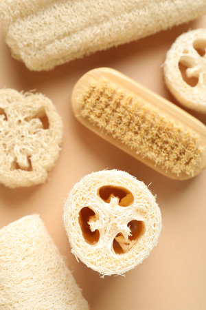 Natural loofah sponges and brush on beige background, flat lay