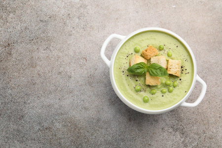 Tasty pea cream soup with croutons and basil on grey table, top view. Space for textの写真素材
