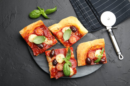 Pieces of tasty homemade pizza and cutter on black table, flat lay