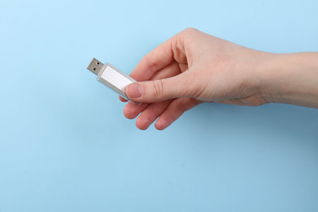 Woman holding USB flash drive on light blue background, closeup