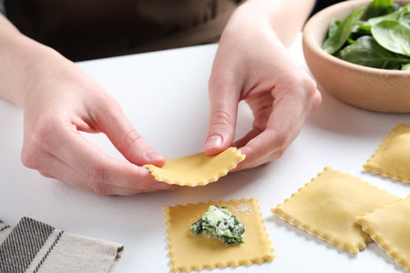 Woman making ravioli with cheese and spinach at white table, closeupの写真素材