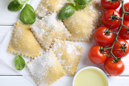 Uncooked ravioli, basil, tomatoes and oil on white wooden table, flat layの写真素材