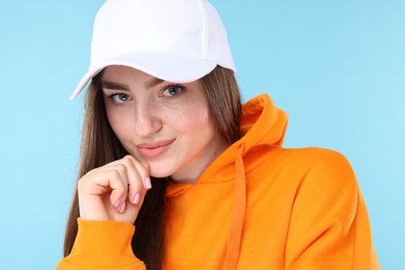 Portrait of beautiful woman in stylish baseball hat on light blue background, closeupの写真素材
