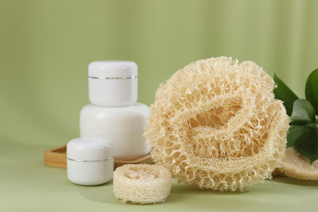 Loofah sponges and jars of cosmetic product on olive background, closeupの写真素材