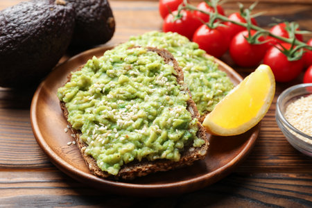 Delicious sandwiches with avocado, sesame seeds, tomatoes and lemon wedge on wooden table, closeupの写真素材