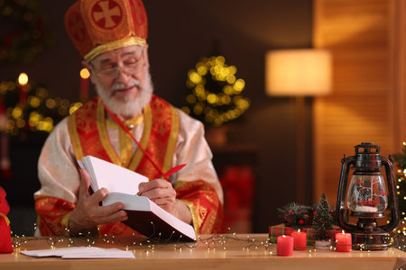 Saint Nicholas with notebook at desk in room decorated for Christmas