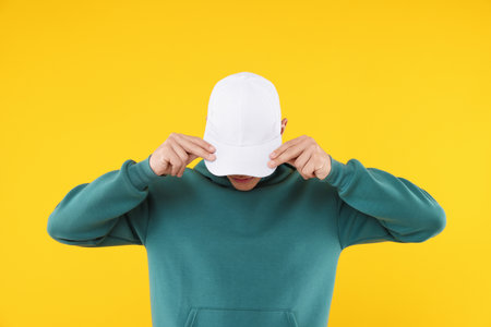 Young man wearing stylish white baseball hat on yellow backgroundの写真素材