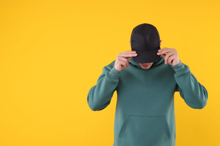 Young man wearing stylish black baseball hat on yellow background, space for textの写真素材