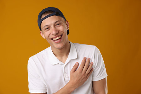 Young man in stylish baseball hat on orange background