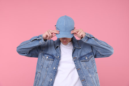 Young man wearing stylish denim baseball hat on pink backgroundの写真素材