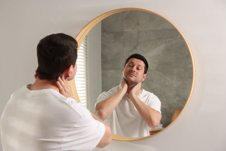 Handsome man looking at himself in mirror indoorsの写真素材
