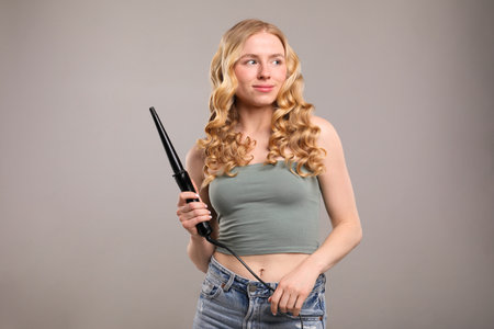 Woman with beautiful hair and curling iron on grey backgroundの写真素材
