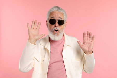Elderly man in stylish outfit on pink background