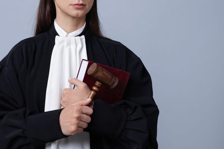 Judge with mallet and book on gray background, closeup. Space for text