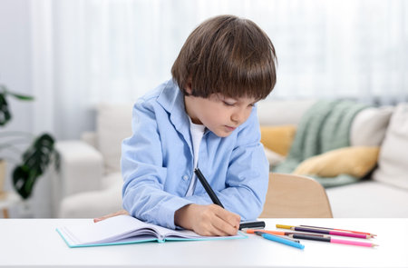 Cute little boy doing homework at table indoors