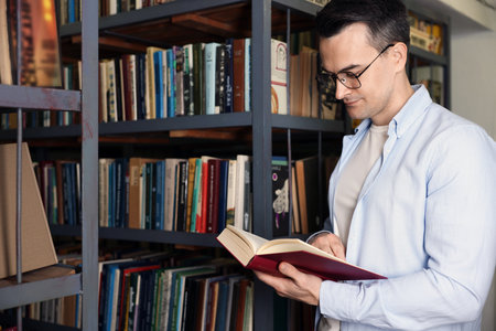 Man reading book near shelves in public libraryの写真素材