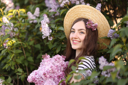 Smiling woman among lilac flowers and leaves outdoorsの写真素材