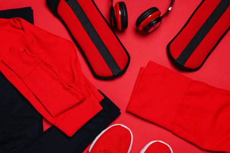 Sportswear, sneakers, ankle weights and headphones on red background, flat layの写真素材