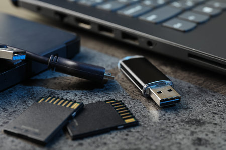 SD memory cards, USB flash drive, hard disk drive with cable and laptop on dark gray table, closeup