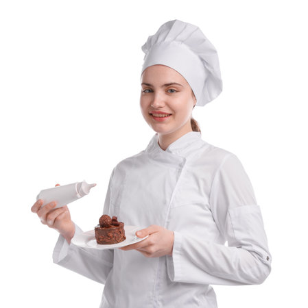 Happy confectioner in uniform holding delicious chocolate dessert and bottle of sauce on white backgroundの写真素材