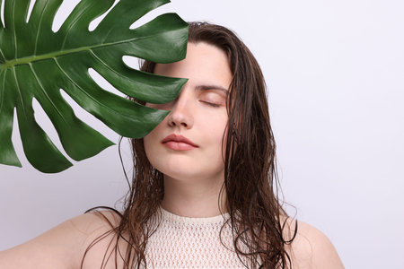 Portrait of beautiful woman with natural skin complexion and monstera leaf on grey background, closeupの写真素材