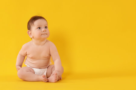 Cute little baby in diaper sitting on yellow background. Space for textの写真素材