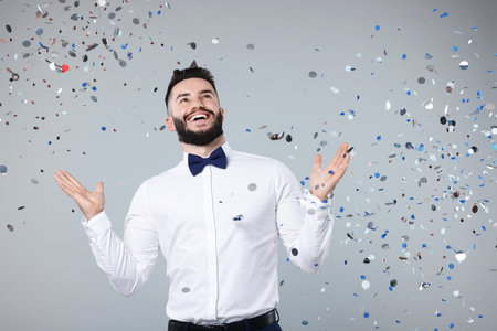 Happy Birthday. Handsome man with party hat under confetti shower on grey background, space for textの写真素材