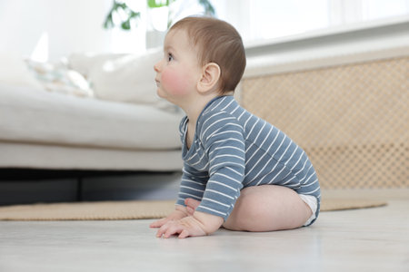 Cute little baby sitting on floor at home