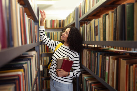 Woman with books and backpack near shelves in public libraryの写真素材