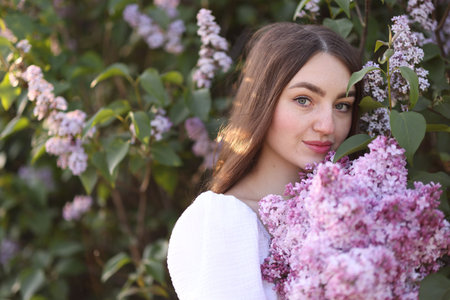 Beautiful woman among lilac flowers and leaves outdoors