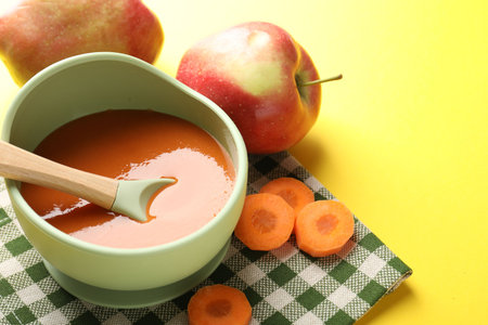 Baby food. Tasty puree in bowl and ingredients on yellow background, closeupの写真素材