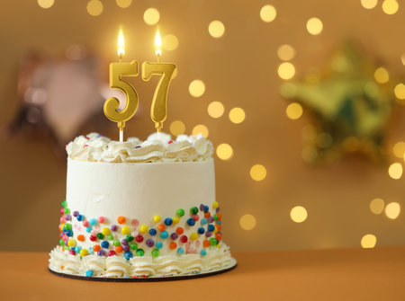 Yummy cake with burning number shaped candles against blurred lights, space for text. 57th birthday or other special occasionの写真素材