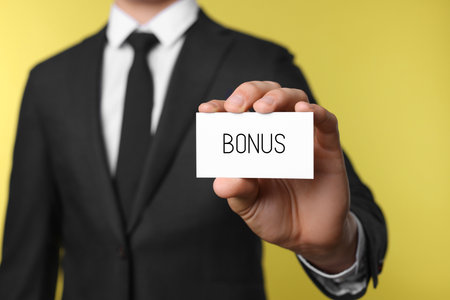 Businessman showing card with word bonus on yellow background, closeupの写真素材