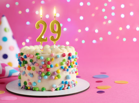 Yummy cake with burning number shaped candles on pink background with blurred lights, space for text. 29th birthday or other special occasionの写真素材